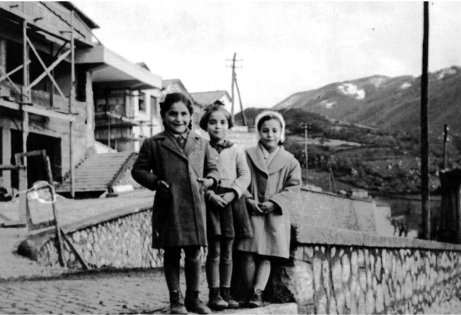 Tre bambine con alle spalle l'edificio scolastico in costruzione in una foto in bianco e nero